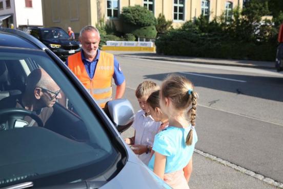 Kinder und ein Polizist im Gespräch mit einem Autofahrer