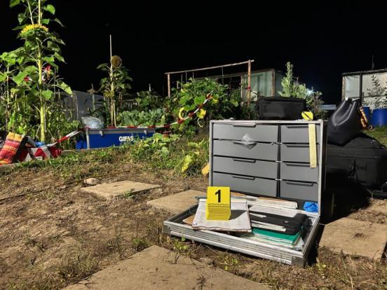 Spurensicherungskoffer steht in einer Gartenanlage auf dem Boden. Im Hintergrund hat es verschiedene Gartenpflanzen.