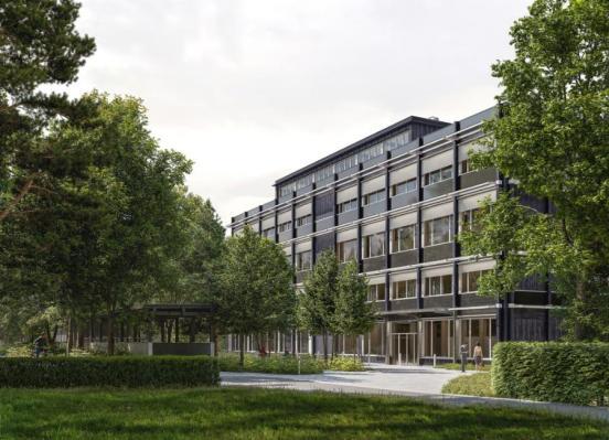 Ein mehrstöckiges, modernes Gebäude mit vielen Fenstern ist von grünen Bäumen und Büschen umgeben. Vor dem Gebäude führt ein Gehweg vorbei und auf dem gepflegten Rasen stehen vereinzelt Menschen.