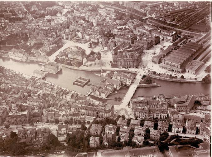 Ein alter, schwarz-weisser Luftbildblick auf eine europäische Stadt. Ein grosser Fluss oder See teilt die Stadt in mehrere Teile, die durch Brucken verbunden sind. 