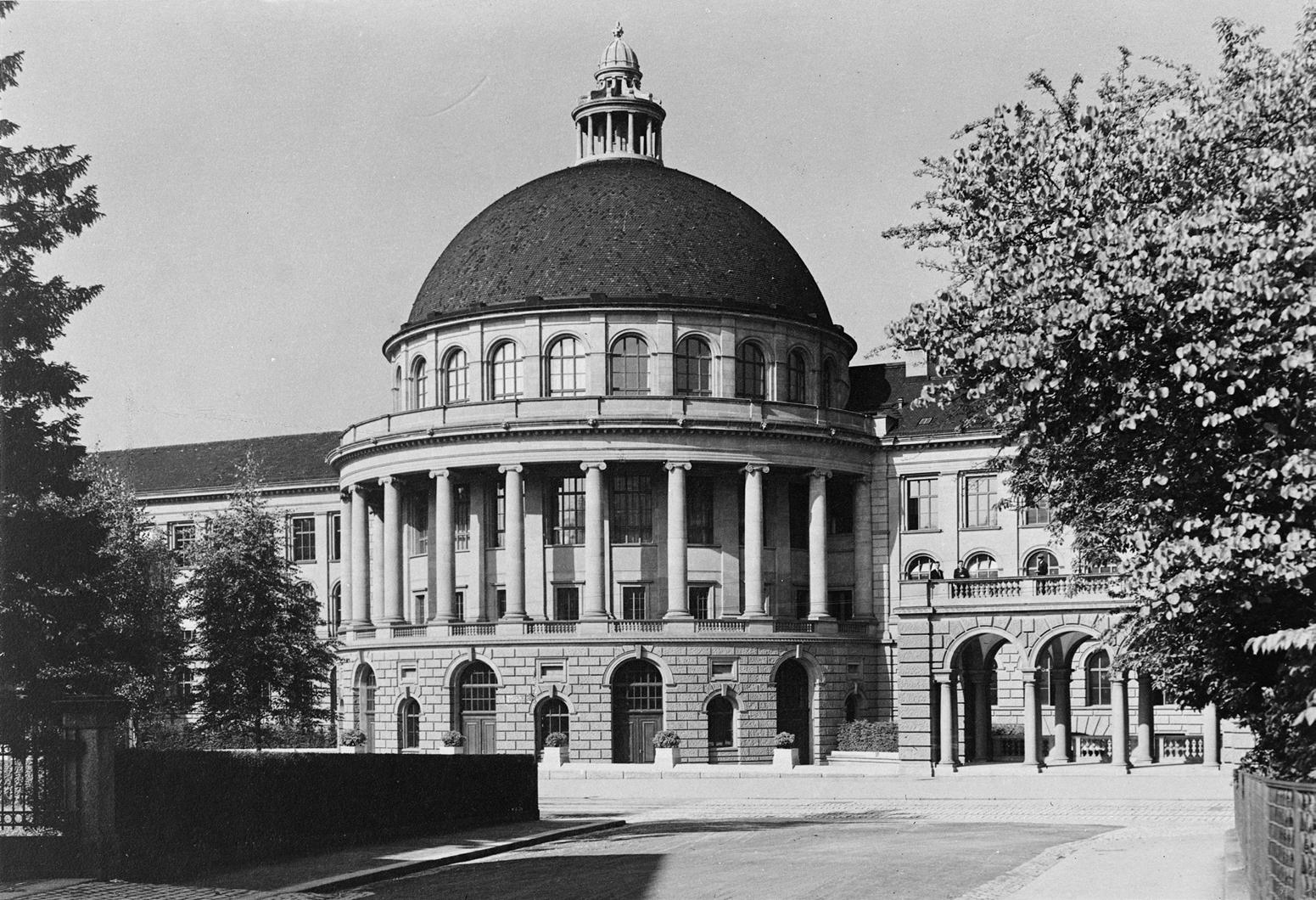 Ein Schwarz-Weiss-Foto eines grossen, majestätischen Gebäudes mit einer imposanten Kuppel. Die Fassade ist im neoklassizistischen Stil gehalten und verfügt über eine Reihe von hohen Säulen. 