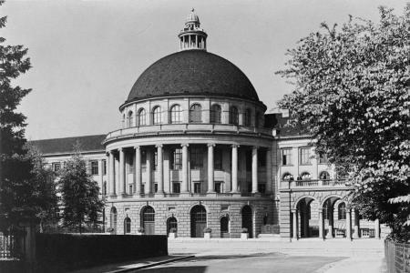 Ein Schwarz-Weiss-Foto eines grossen, majestätischen Gebäudes mit einer imposanten Kuppel. Die Fassade ist im neoklassizistischen Stil gehalten und verfügt über eine Reihe von hohen Säulen. 