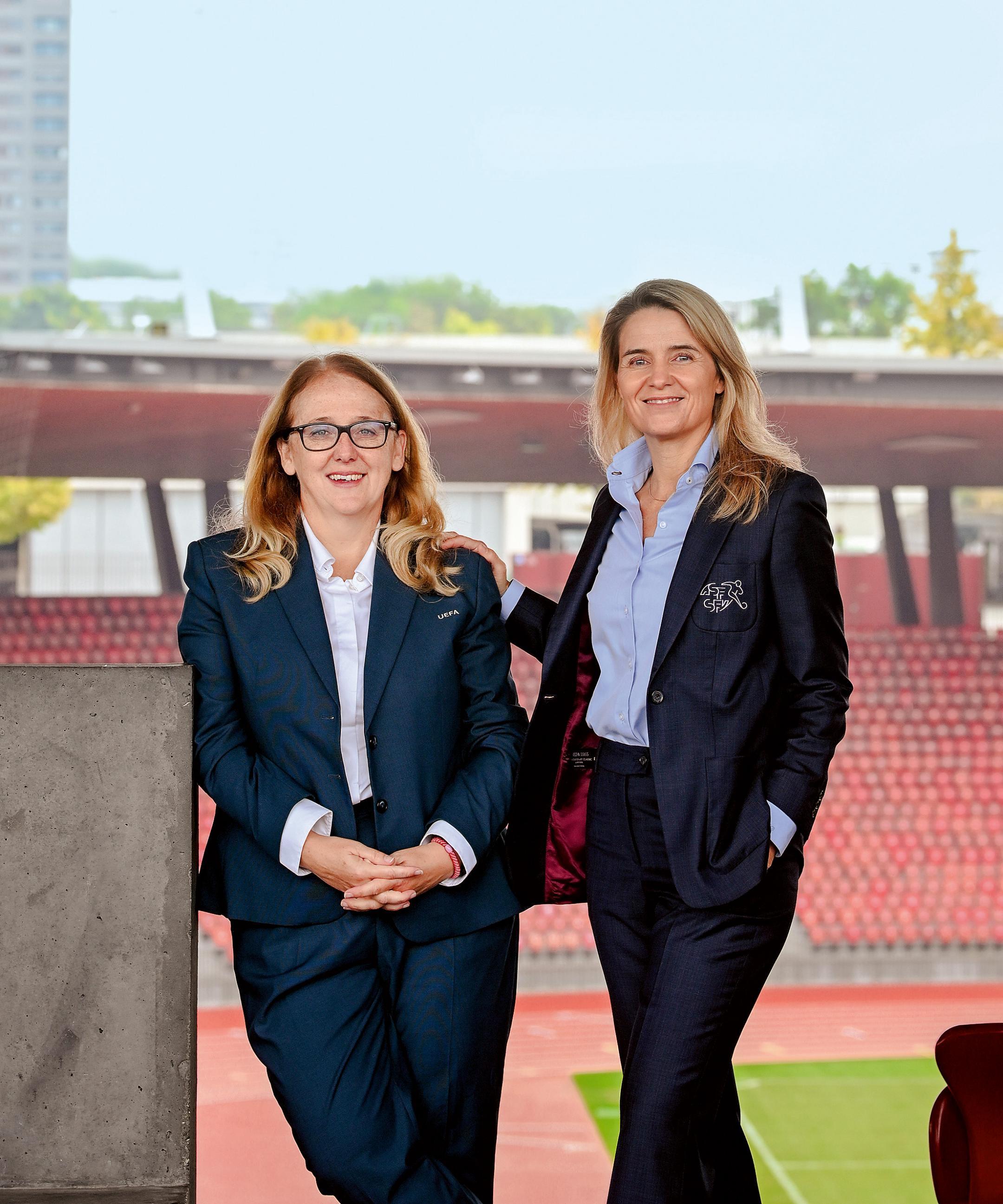 Zwei Frauen in Anzug stehen an eine Mauer in einem 
