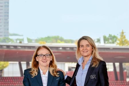 Zwei Frauen in Anzug stehen an eine Mauer in einem 