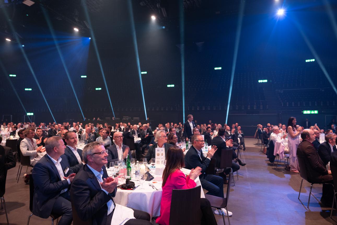 Viele Menschen sitzen um verschiedene Tische und applaudieren