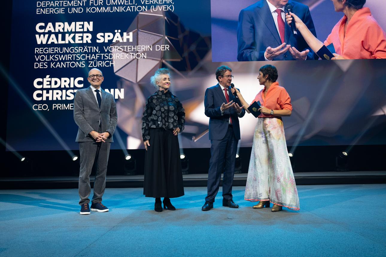 Cédric Christmann, CEO von Primeo Energie, die Zürcher Regierungsrätin Carmen Walker Späh und Bundesrat Albert Rösti stehen auf der Bühne. Rösti wird von einer Moderatorin interviewt.