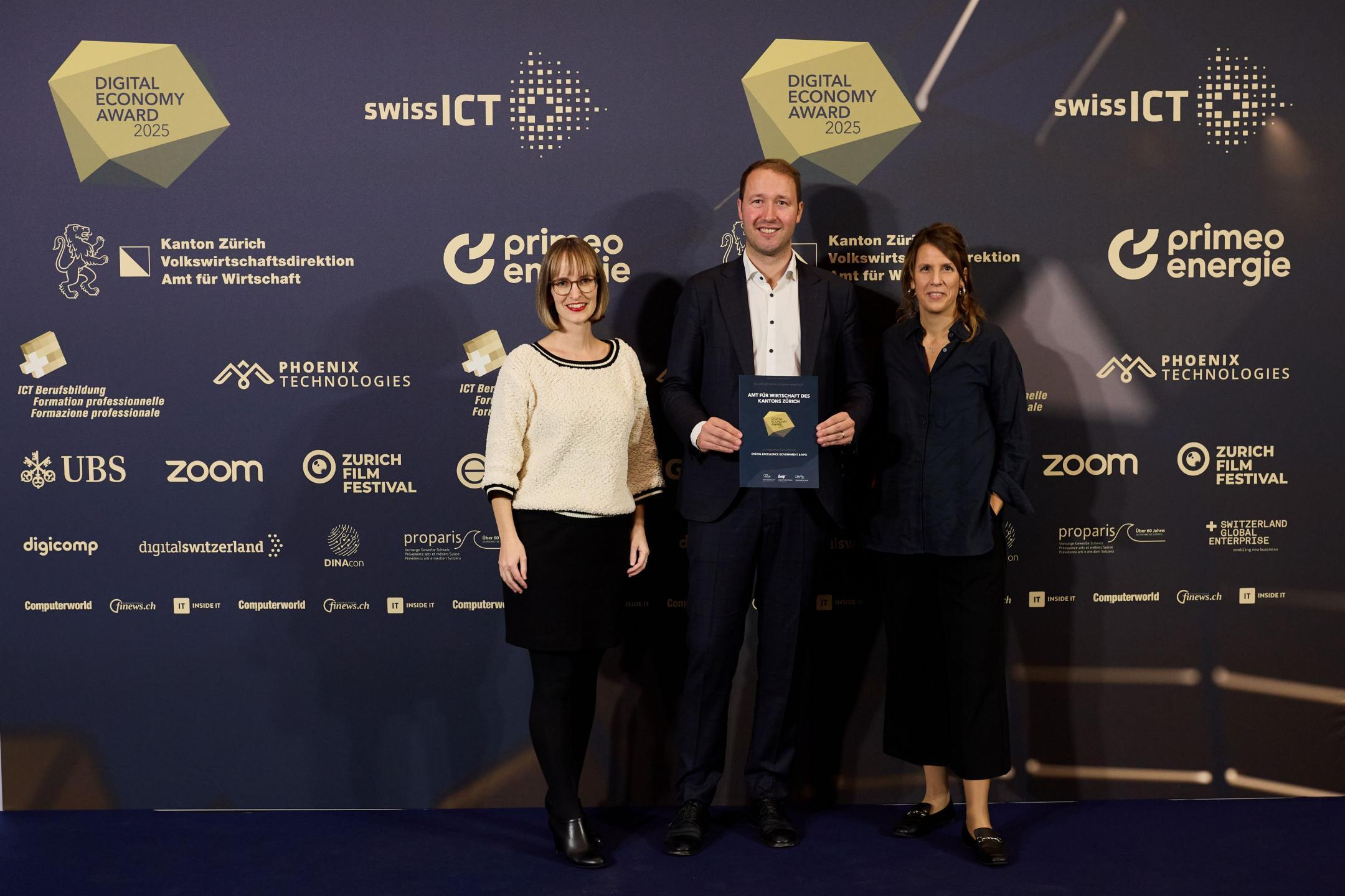 Drei Personen halten die gewonnene Auszeichnung in der Hand und strahlen in die Kamera.