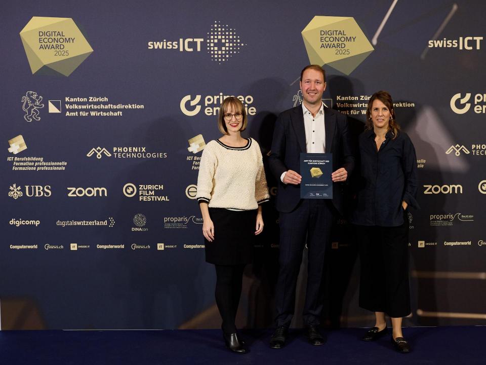 Drei Personen halten die gewonnene Auszeichnung in der Hand und strahlen in die Kamera.