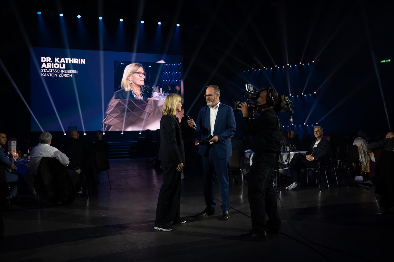 Staatsschreiberin Kathrin Arioli wird von einem Moderator interviewt und wird dabei von einer Kameramann gefilmt