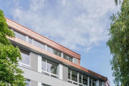 Aussenansicht des Gebäudes mit einheitlich gestalteter Fassade in Grautönen und Bäumen rundherum.