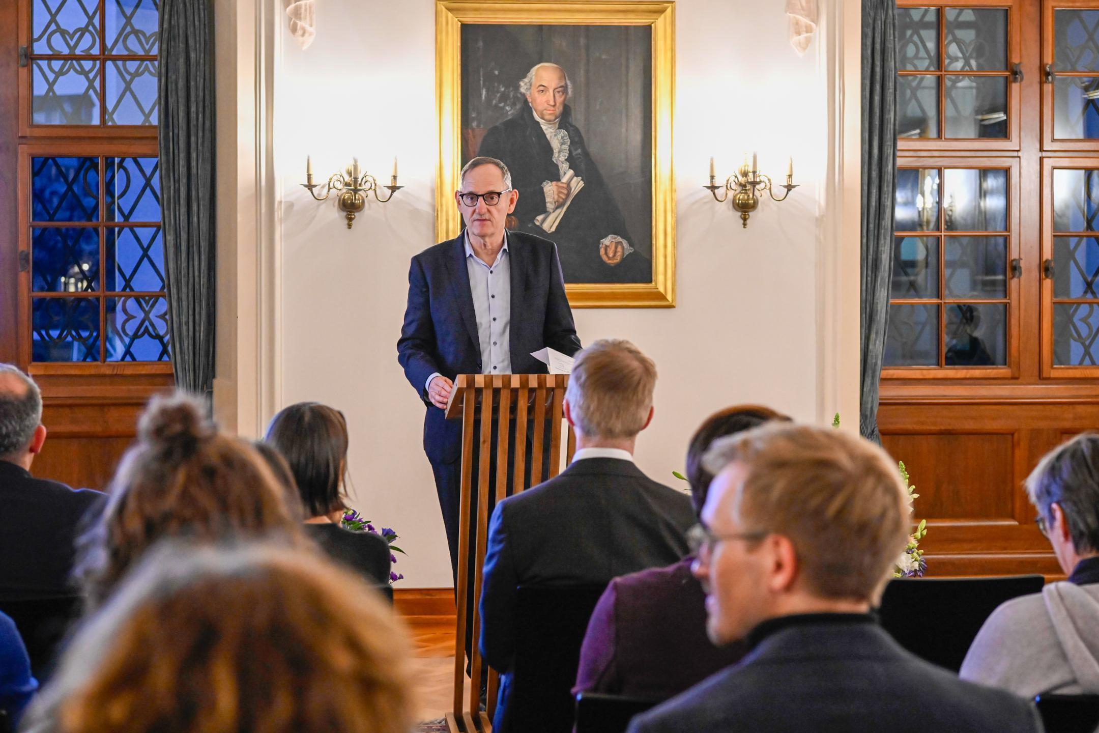 Ein Mann in Anzug spricht an einem Pult aus Holz, im Hintergrund ist ein Bildschirm mit Sportpreis Kanton Zürich zu sehen.