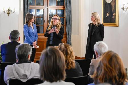 Eine Frau mit langen, braunen Haaren spricht mit zwei blonden Frauen, die links und rechts von ihr stehen.
