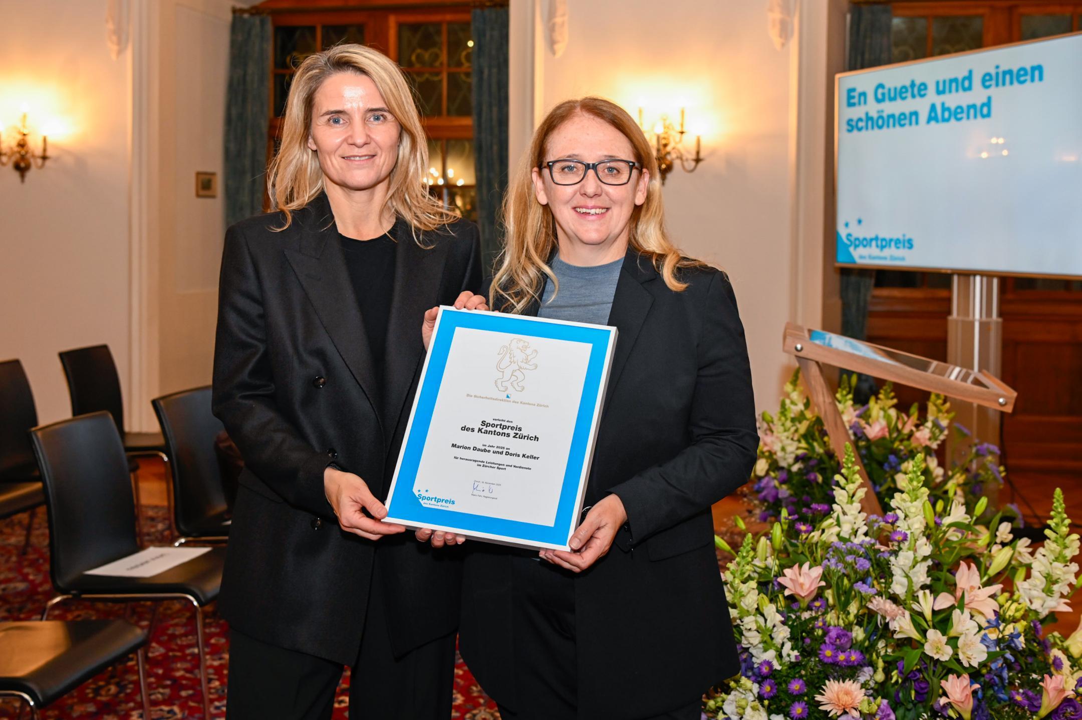 Zwei Frauen mit blonden Haaren posieren mit Urkunde und Blumen in der Hand.
