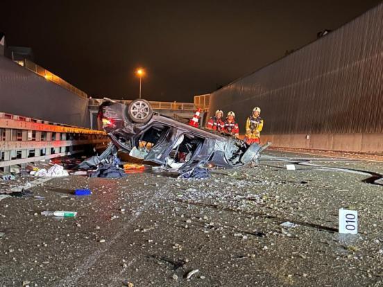Unfallfahrzeug liegt auf dem Dach auf einer Autobahn. Daneben stehen drei Feuerwehrleute