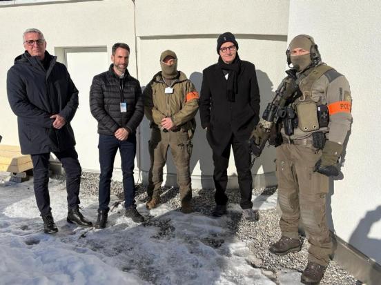 Drei zivil gekleiedete Männer stehen neben zwei bewaffneten Polizisten