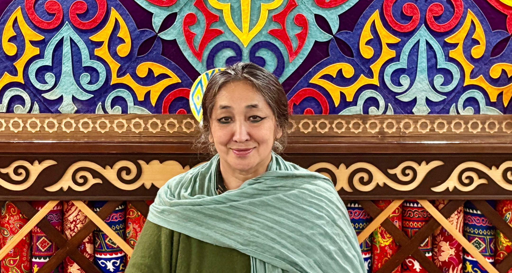 Saadet Türköz, Portrait einer Frau mit schwarzen langen Haaren, im Hintergrund ist ein farbenfrohes Bild.