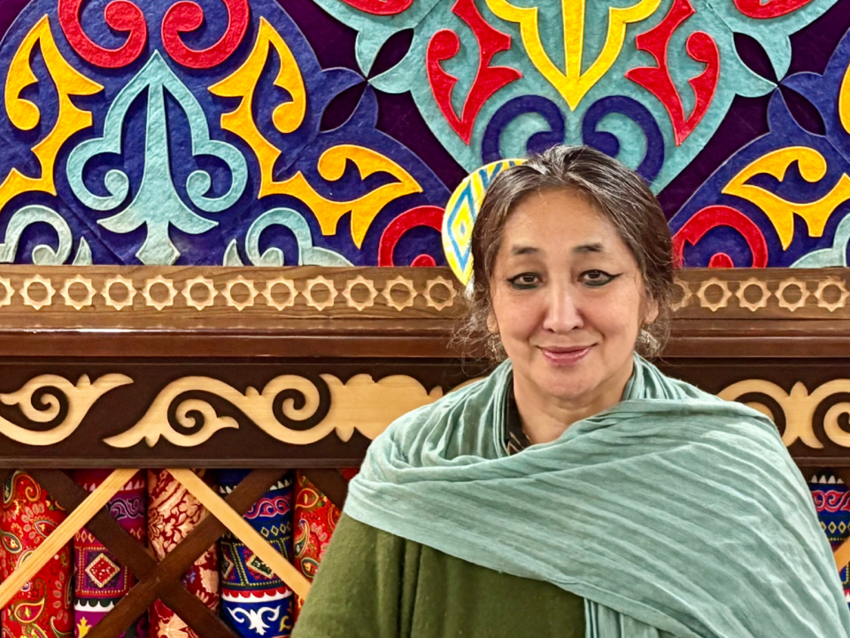 Saadet Türköz, Portrait einer Frau mit schwarzen langen Haaren, im Hintergrund ist ein farbenfrohes Bild.