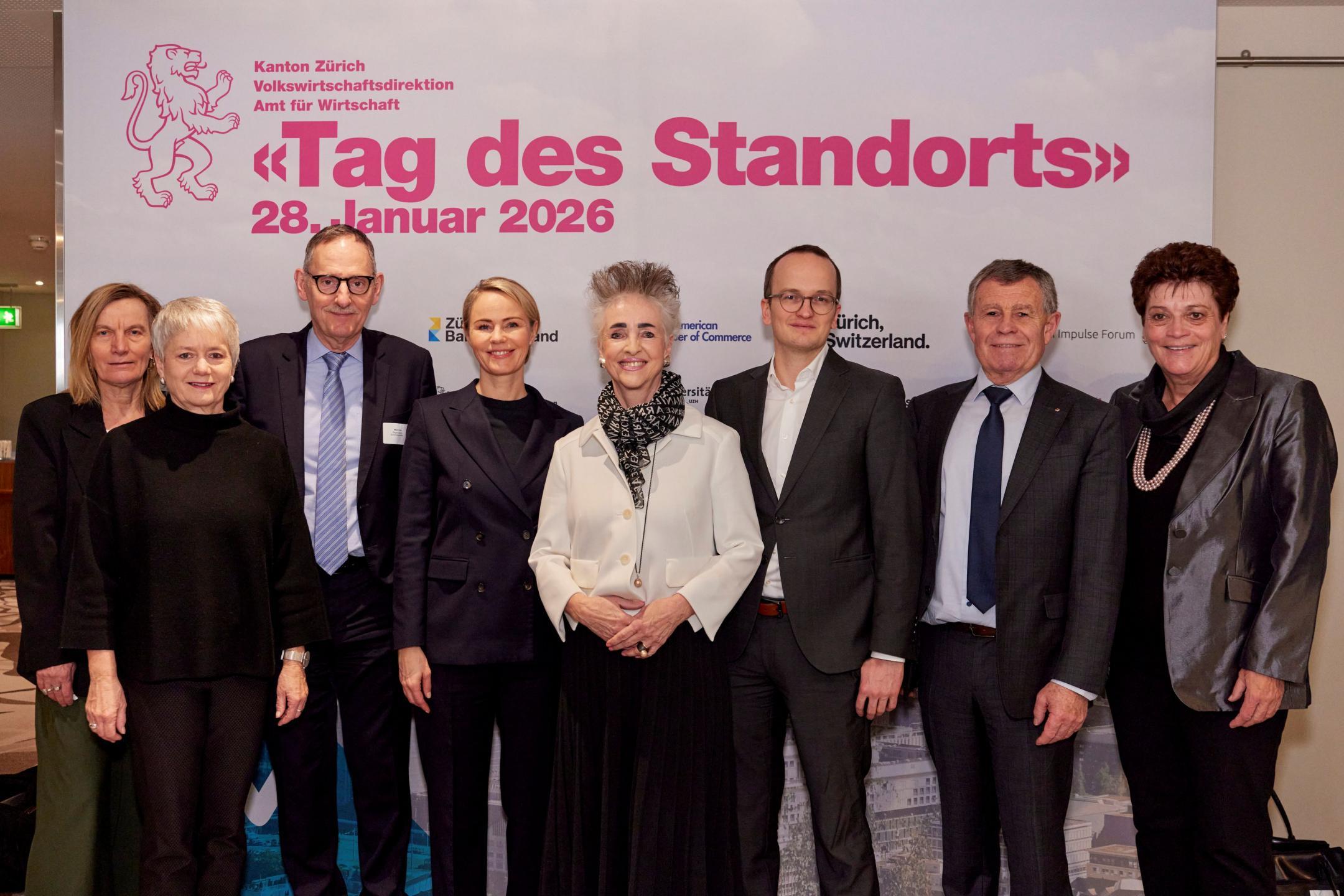 Der gesamte Zürcher Regierungsrat posiert vor einem Plakat mit der Aufschrift «Tag des Standorts 2026»