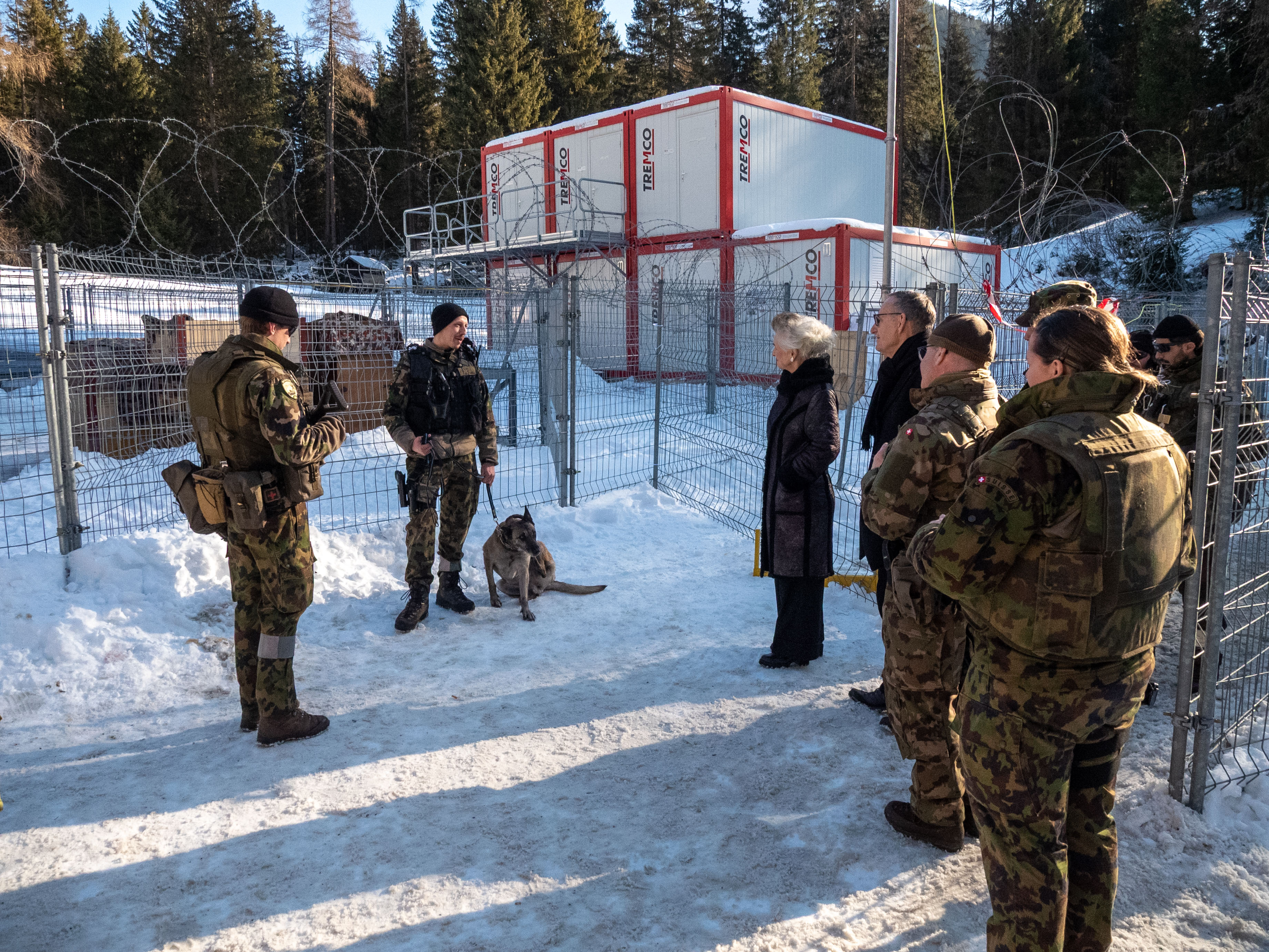 Ein Hundeführer der Schweizer Armee steht vor einem Zaun. Er ist im Gespräch mit den Regierungsräten und weiteren Armeeangehörigen.