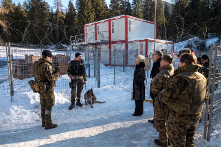 Ein Hundeführer der Schweizer Armee steht vor einem Zaun. Er ist im Gespräch mit den Regierungsräten und weiteren Armeeangehörigen.