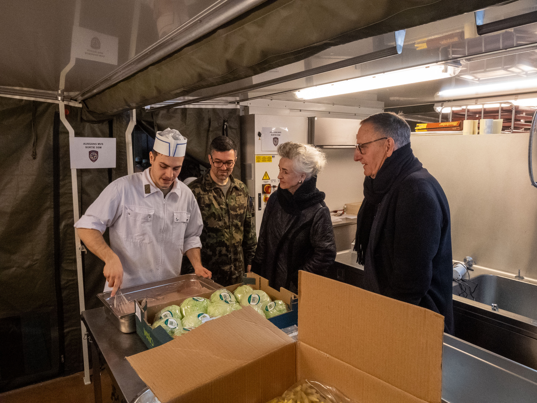 Ein Koch der Schweizer Armee steht in der Küche vor einer Kiste Esswaren.