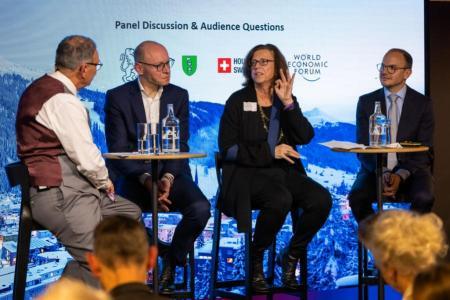 Drei Männer und eine Frau sitzen an Stehtischen auf dem Podium und diskutieren