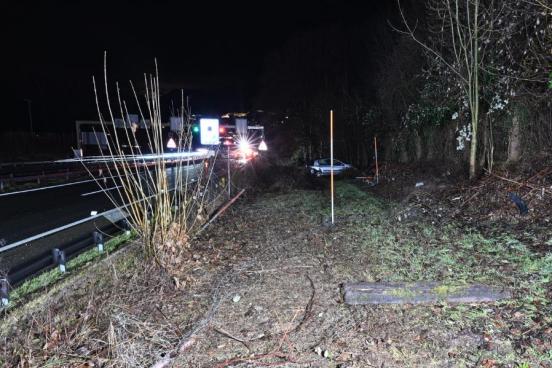 Trümmerteile und im Hintergrund ein beschädigtes Auto  neben der Autobahn, nachts.