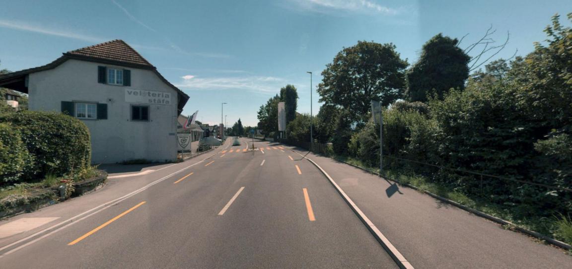 Farbaufnahme einer Strasse mit gelben Markierungen in Stäfa, flankiert von einem weissen Gebäude und dichter Begrünung.