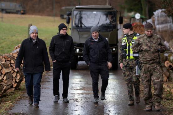 Sicherheitsdirektor Mario Fehr und Stadtpräsident Marco Nuzzi sind umrahmt von mehreren Personen. Sie laufen auf den Fotografen zu. Dahinter steht ein Panzer. Alle tragen Outdoor-Kleidung.