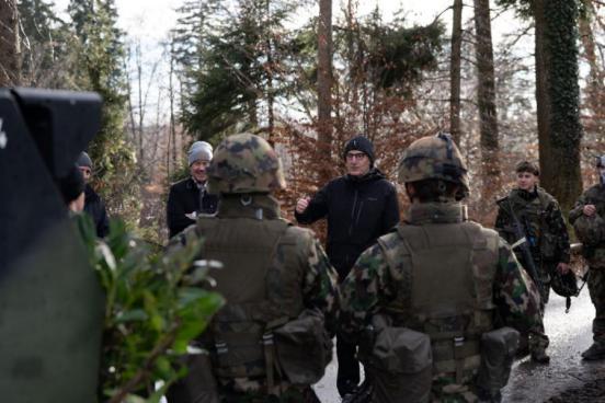 Sicherheitsdirektor Mario Fehr spricht zu einer kleinen Gruppe Soldaten, welche um ihn herumstehen. Sie stehen in einem Wald.