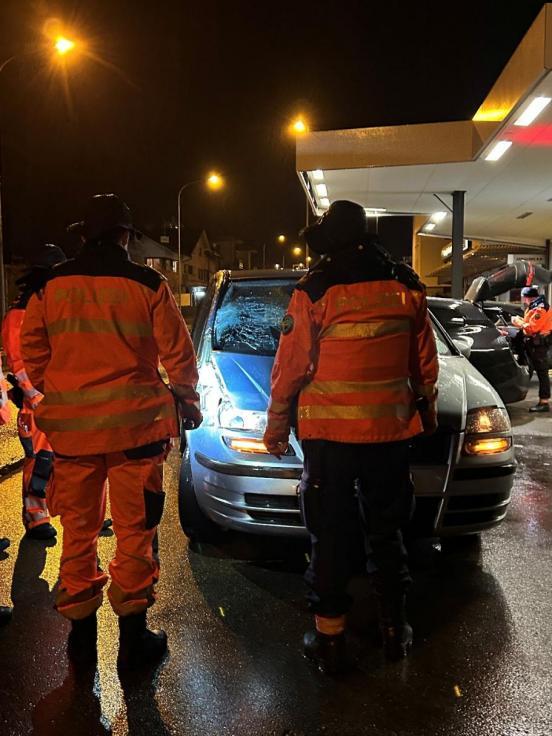 zwei Polizisten stehen vor einem an der Windschutzscheibe beschädigten Auto.