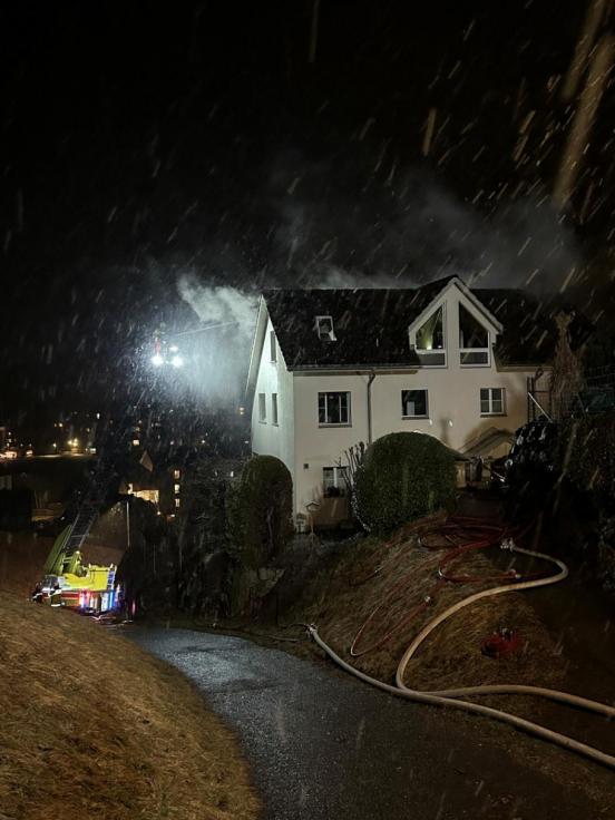Wohnhaus bei Nacht. Daneben steht eine Feuerwehrauto und Feuerwehrschläuche führen zum Haus.