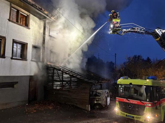 Zwei Feuerwehrleute auf einer Drehleiter lenken Wasserstrahl gegen das Feuer 