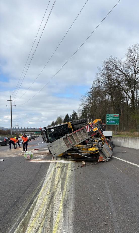 Ein gekippter Anhänger mit einem Radbagger. Die Autobahn ist stark verschnutzt.