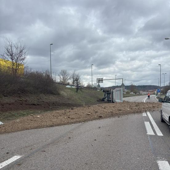 Ein Lastwagen liegt auf der Autobahn auf der Seite und die geladene Erde ist auf der Fahrbahn verstreut