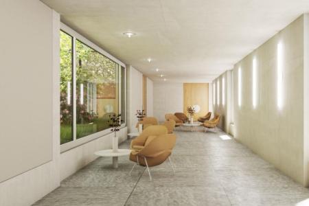 Langer Flur mit sandfarbenen Lounge-Sesseln an runden Tischen, grosse Fenster mit Blick auf eine Grünfläche und dezenter Wandbeleuchtung.