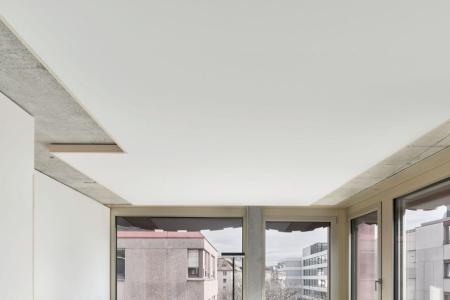 Modernes Bürozimmer mit hellblau-grauem Boden, einem schwarzen Büromöbel, weissem Schreibtisch und Bürostuhl vor grossem Fenster. 