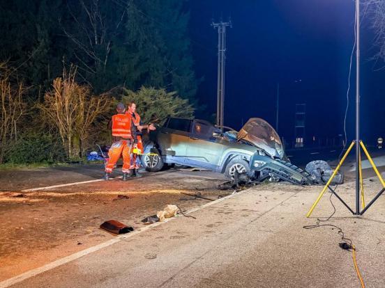 Zwei Polizsiten stehen nachts neben einem Unfallaufto das quer auf der Strasse steht.