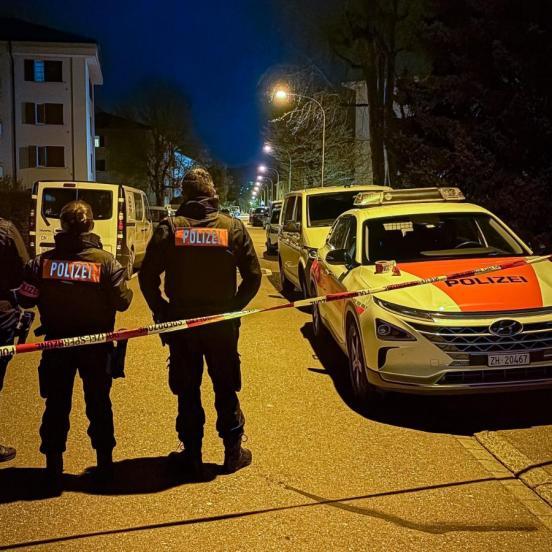 Zwei Polizisten stehen auf einer Strasse  neben einem Polizeiauto