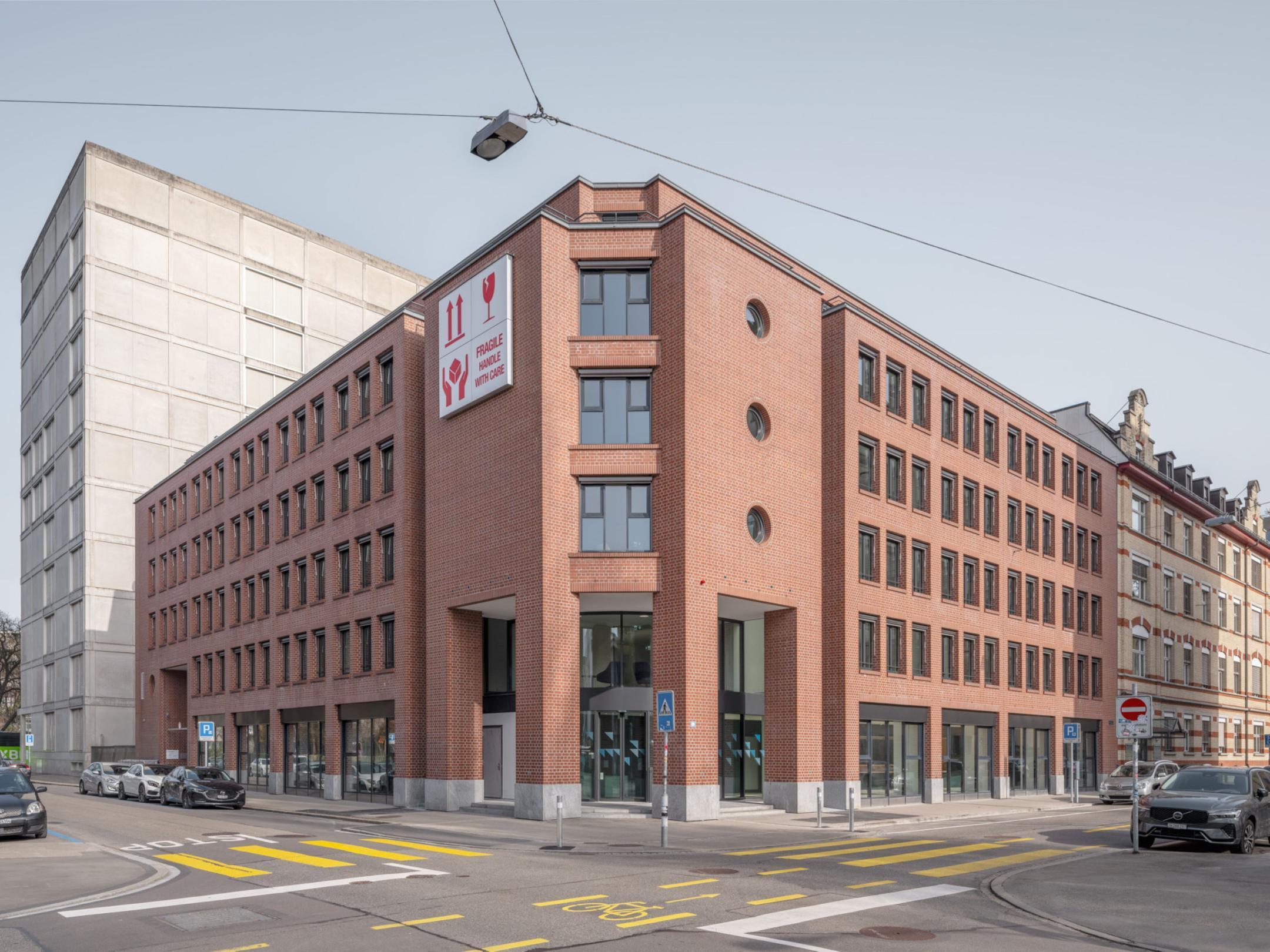 Aussenansicht von einem Bürogebäude. Die Fassade ist rot/braun. Das Gebäude steht an einer Strasse.