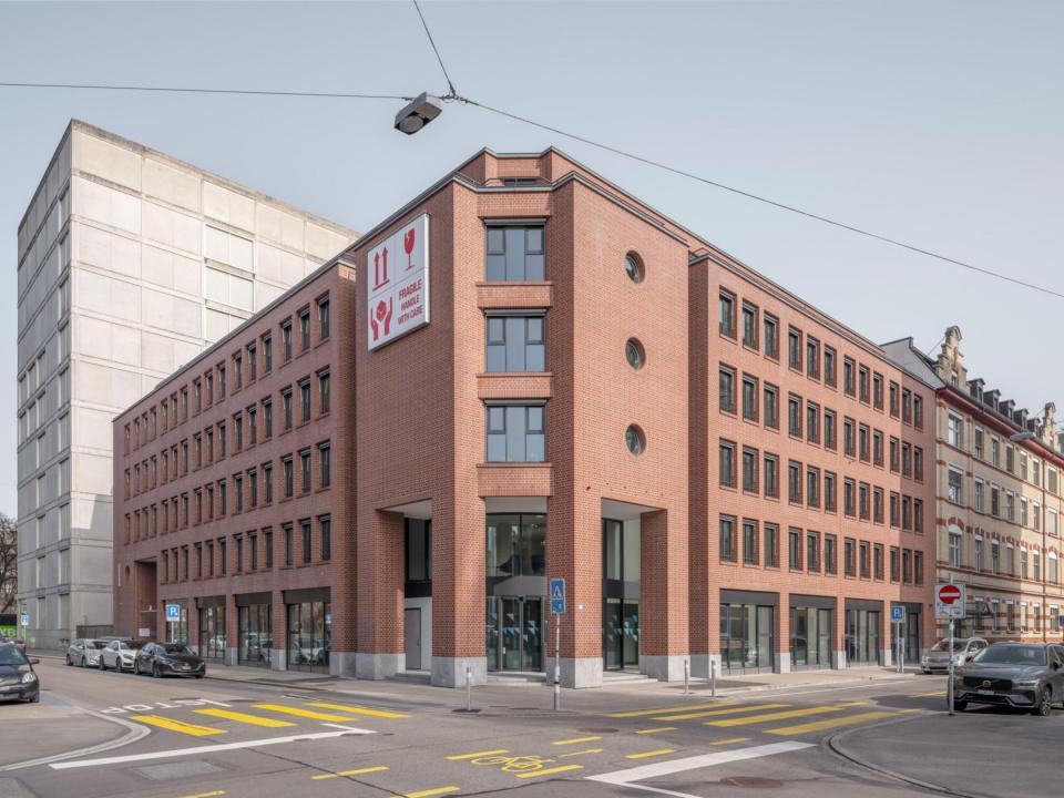 Aussenansicht von einem Bürogebäude. Die Fassade ist rot/braun. Das Gebäude steht an einer Strasse.