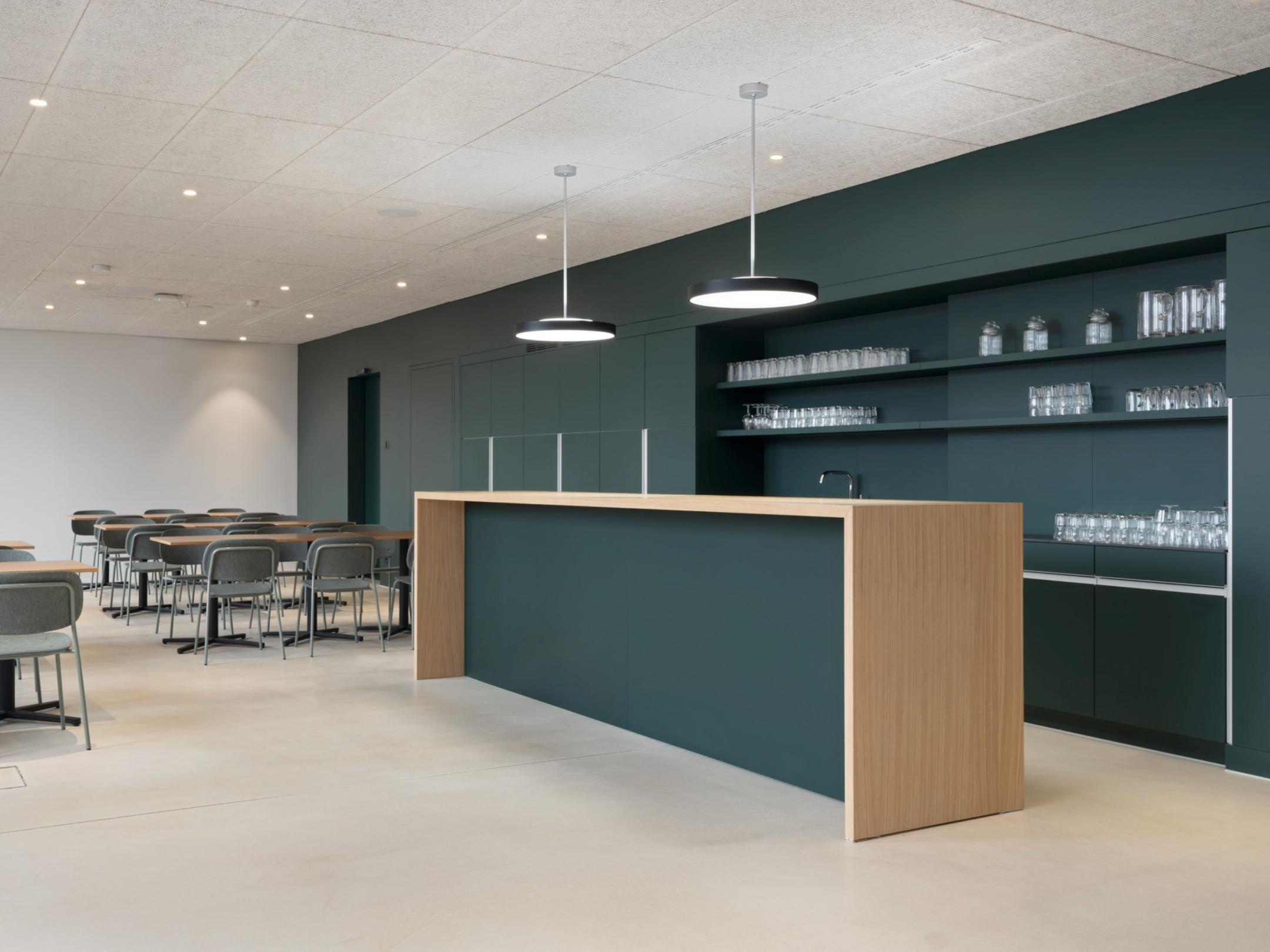 Moderne Teeküche mit dunkelgrüner Theke, Holzverkleidung und Sitzbereich.