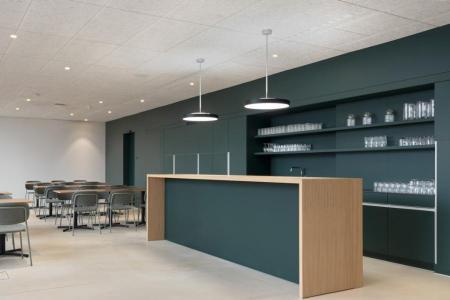 Moderne Teeküche mit dunkelgrüner Theke, Holzverkleidung und Sitzbereich.