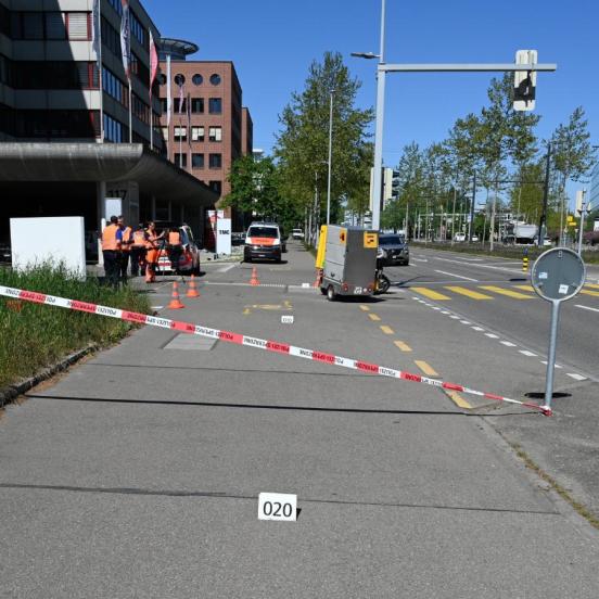 Ein Radweg neben einer Strasse der mit einem rotweissen Band abgesperrt ist. Dahinter steht ein dreirädriges Kleinmotorfahrzeug mit Anhänger und daneben stehen Polizisten.