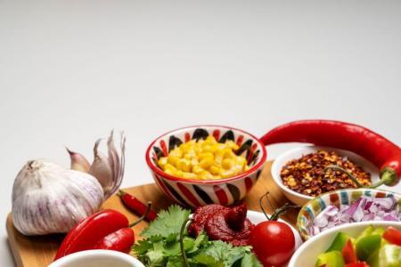 Verschiedene Zutaten wie Hackfleisch, Gemüse, Gewürze und Kräuter für die Zubereitung eines Chili-Gerichts auf einem Holzbrett.