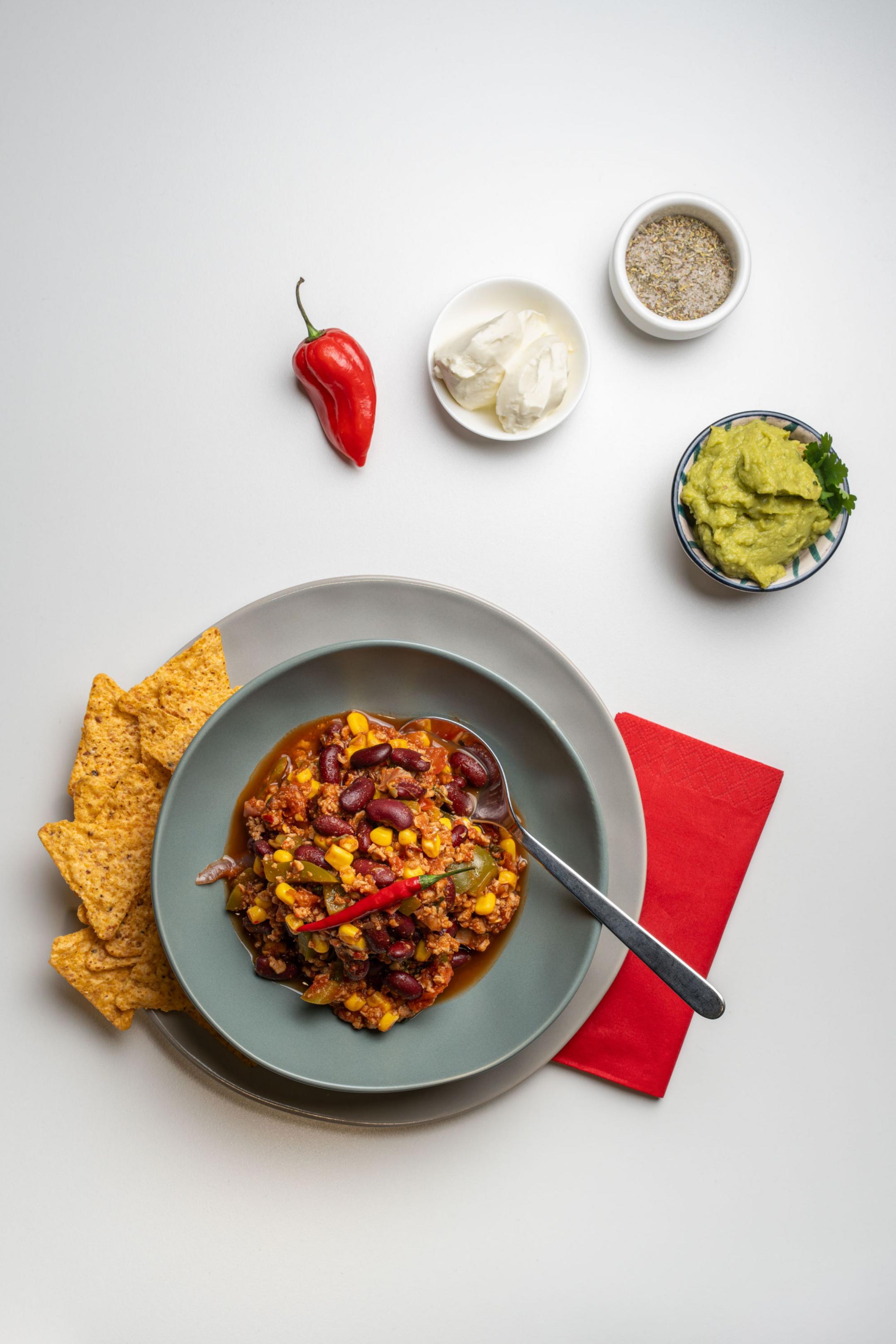 Schale mit Chili sin Carne aus Bohnen, Mais und Gemüse, serviert mit Tortilla-Chips und Beilagen.
