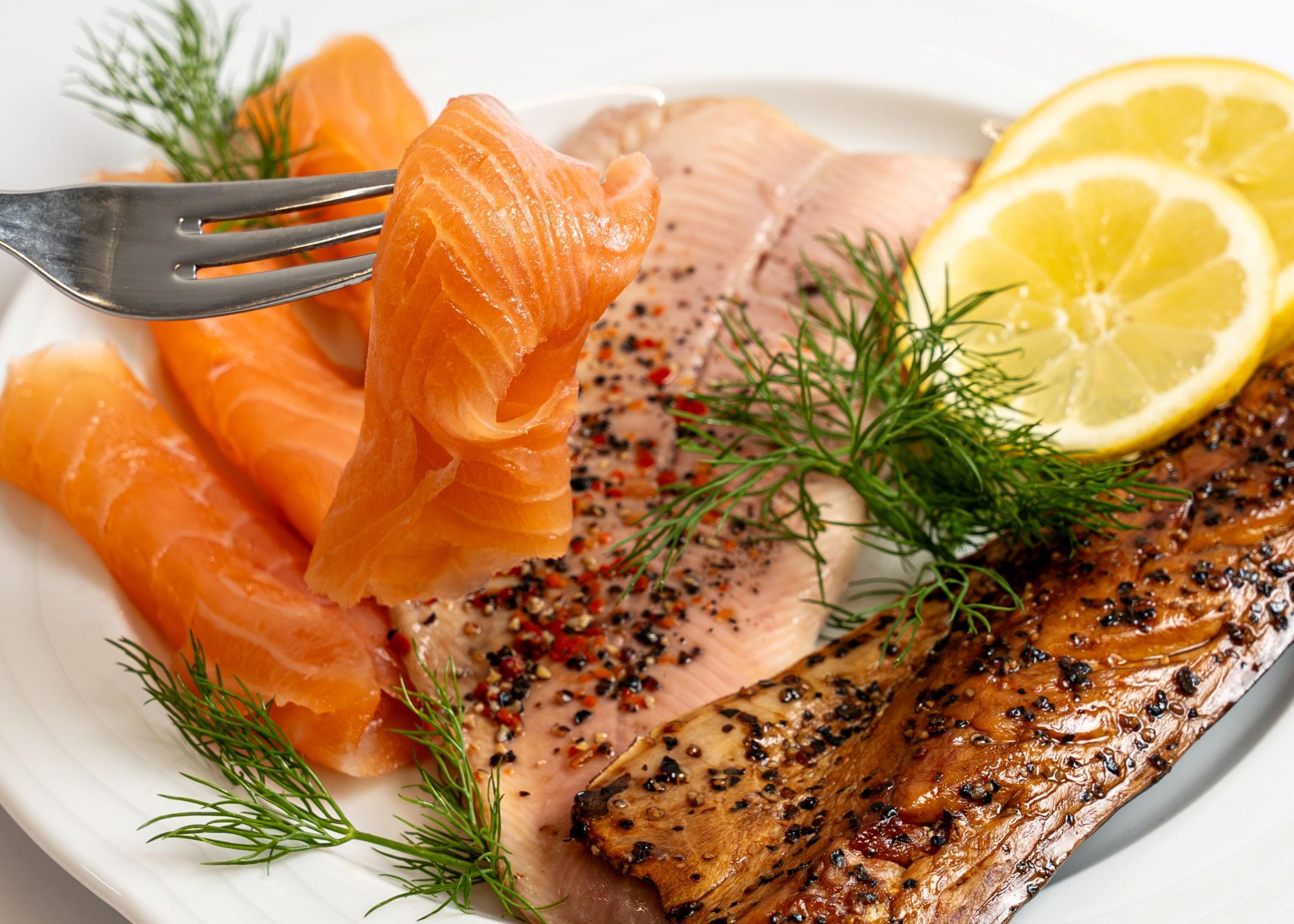 Verschiedene Fischproben, darunter roher und gegarter Fisch, mit Gewürzen und Zitrone angerichtet.