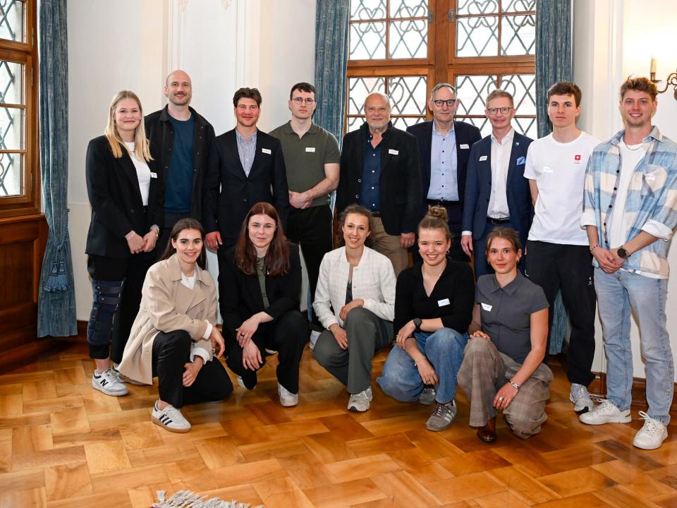 Ein Gruppe sportlicher Menschen in eleganter Kleidung posiert in einem Festsaal zusammen mit drei Männern.