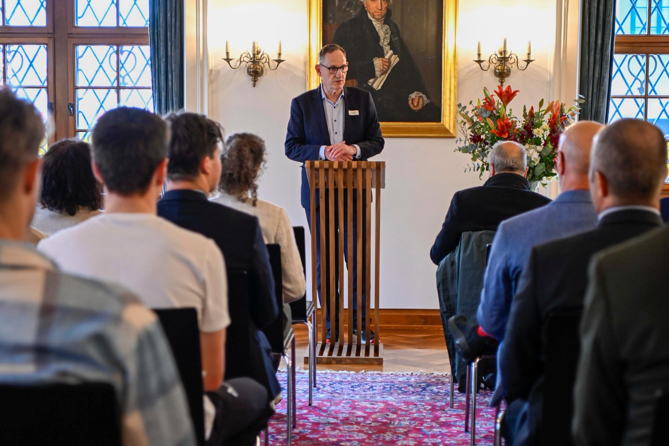 Ein Mann mit Brille uns Schnauz spricht an einem Rednerpult.