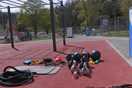 Outdoor-Fitnessbereich mit Trainingsgeräten und einer blauen SportBox mit der Aufschrift «Fit!?».